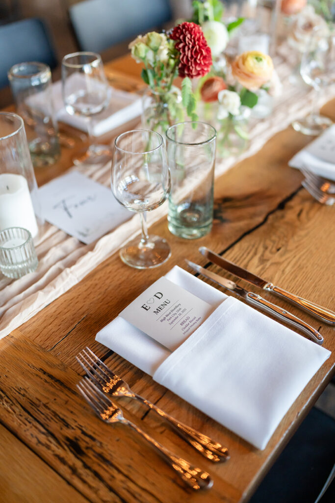 Elegant wedding place setting with custom menu card, white linen napkin, blush gauze runner, floral centerpiece, and polished flatware at a luxury destination wedding at High West Distillery in Park City, Utah, planned by Shellie Ferrer Events.