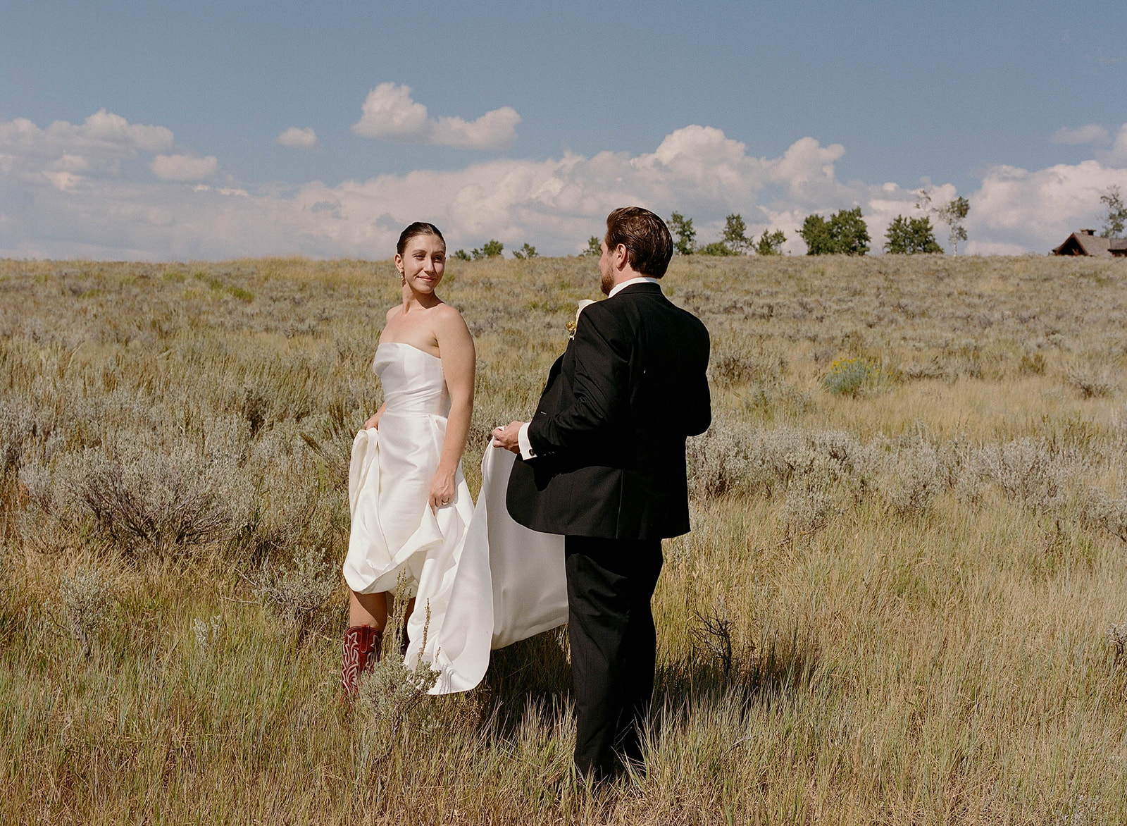 Bride in a strapless wedding gown revealing red embroidered cowboy boots while walking through a meadow with the groom at a private residence wedding on Wolfe Creek Ranch Road in Utah, planned by Shellie Ferrer Events.