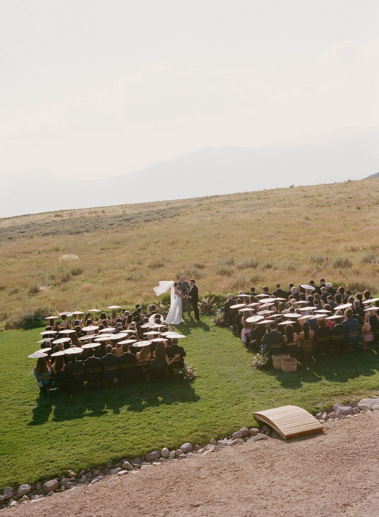 Aerial view of a destination luxury wedding ceremony with guests, floral aisle arrangements, and mountain views at a private residence on Wolfe Creek Ranch Road in Utah, planned by Shellie Ferrer Events.