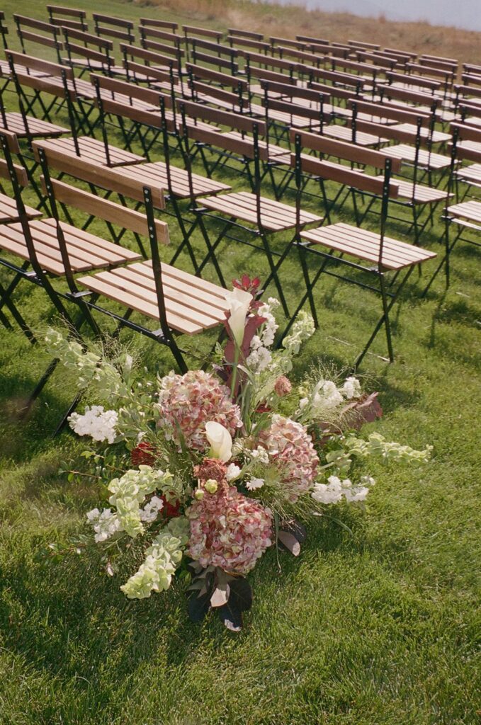 Outdoor wedding ceremony seating with wooden chairs and organic floral aisle arrangements at a private residence destination wedding off Wolfe Creek Road in Utah, planned by Shellie Ferrer Events.
