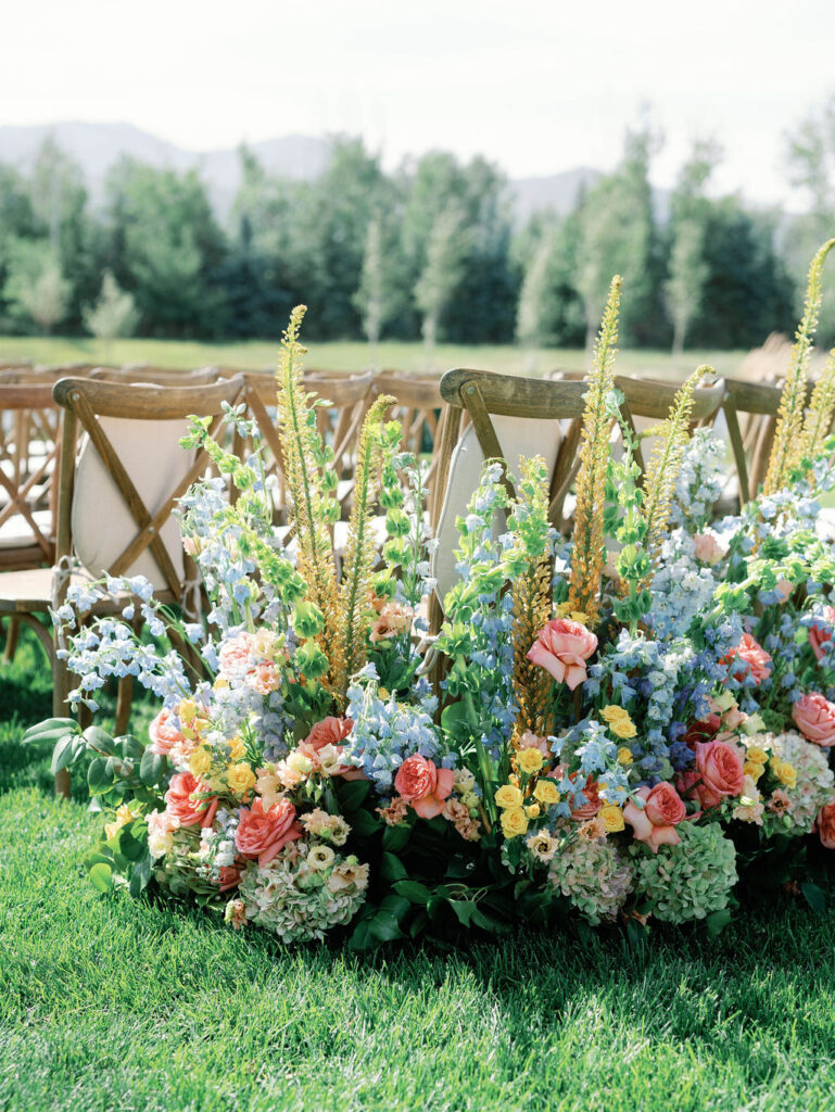 Rustic wooden guest seating lined with lush garden-inspired florals along the ceremony aisle at 4U Ranch in Peoa, Utah, planned by Shellie Ferrer Events.
