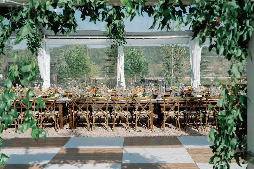 Elegant wedding reception tablescape with colorful florals, lush greenery, candlelight, and farmhouse tables inside a clear-top tent at 4U Ranch in Peoa, Utah, planned by Shellie Ferrer Events.