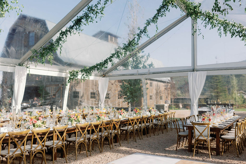 Luxury destination wedding reception inside a clear-top tent with farmhouse tables, colorful florals, hanging greenery, and mountain views at 4U Ranch in Peoa, Utah, planned by Shellie Ferrer Events.