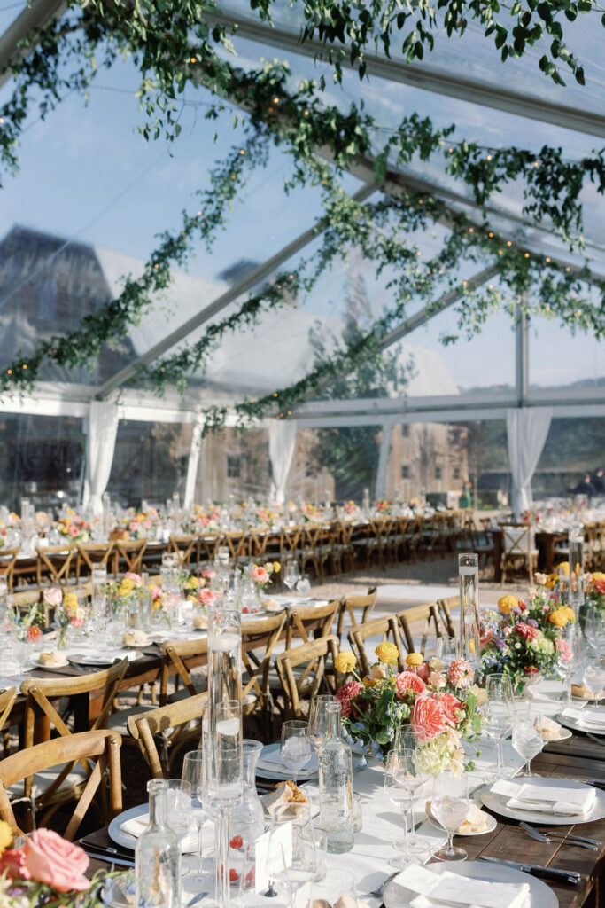 Farmhouse wedding reception tables with colorful florals, floating candles, and hanging greenery inside a clear-top tent at 4U Ranch in Peoa, Utah, planned by Shellie Ferrer Events.