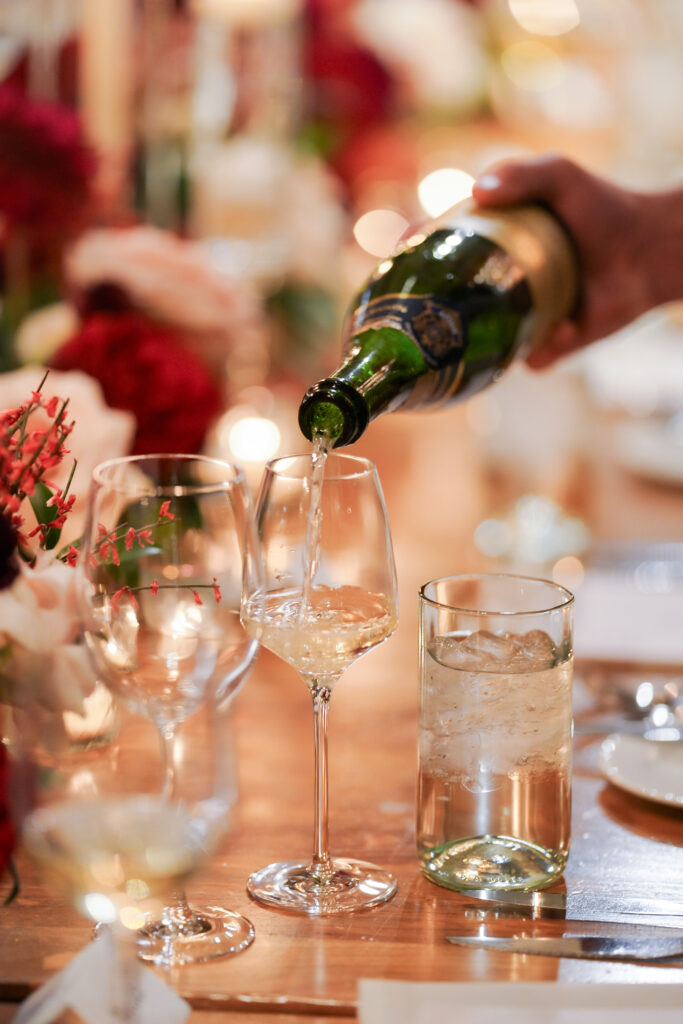 Wine being poured during an intimate wedding dinner at St. Regis Deer Valley featuring abundant red and ivory floral tablescapes, candlelight, and elegant reception décor planned by Shellie Ferrer Events.