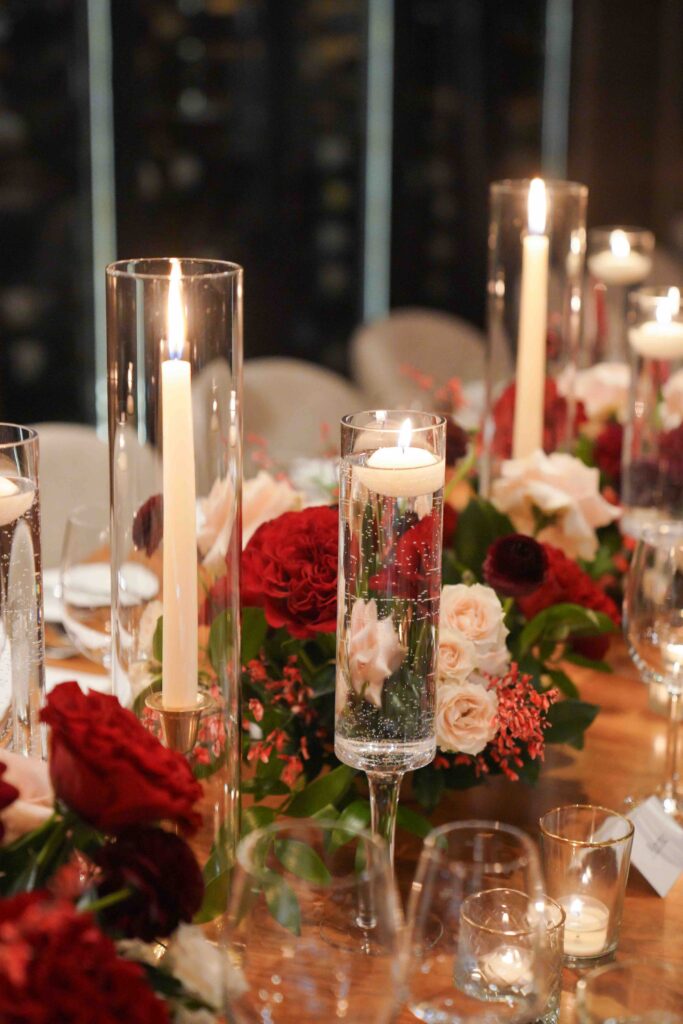 Romantic Valentine's Day wedding tablescape in the Wine Vault at St. Regis Deer Valley featuring floating tea lights in champagne glasses, candlelight, and red, blush, and ivory floral arrangements.