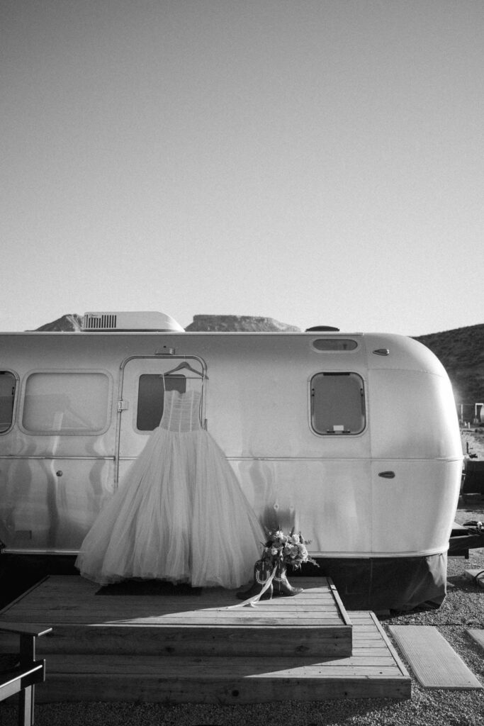 Black and white wedding photo of a wedding dress hanging on an Airstream trailer with a bridal bouquet at AutoCamp Zion in Utah.