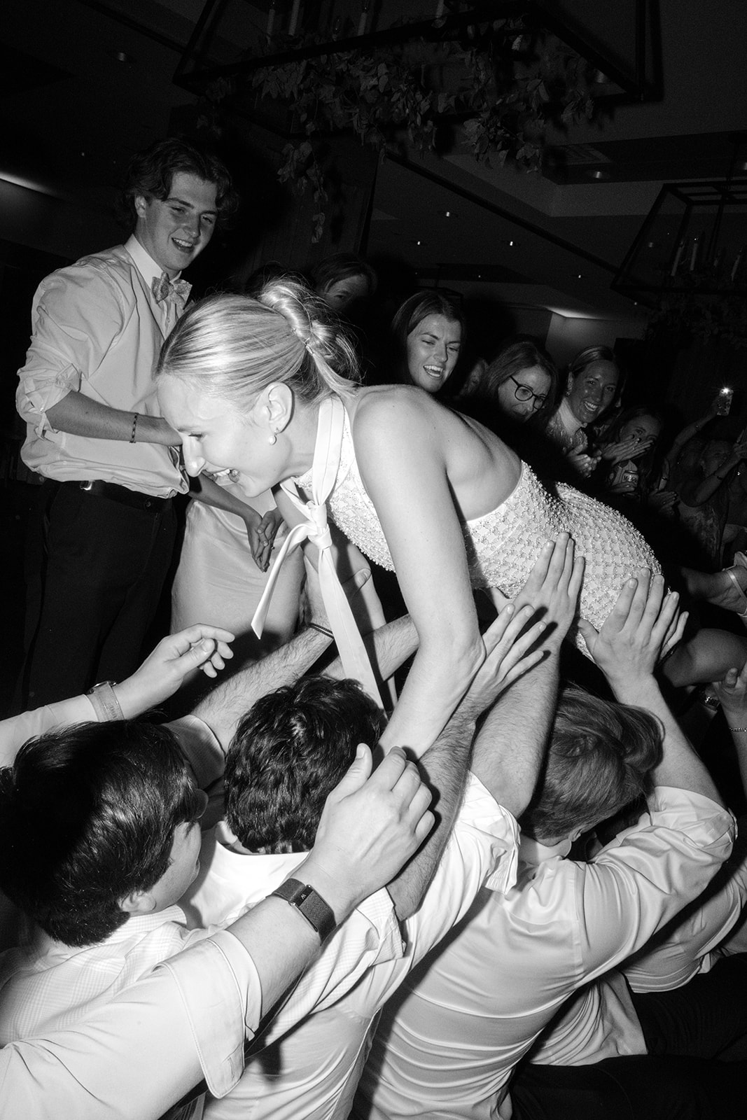 Black-and-white photograph of the bride crowd surfing above wedding guests during her Snowpine Lodge reception in Little Cottonwood Canyon, Utah.