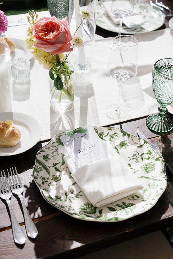 Elegant wedding place setting with green botanical dinnerware, personalized menu and coral rose centerpiece at Snowpine Lodge in Utah.