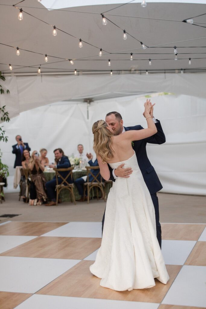 Bride and groom sharing their first dance beneath string lights at a tented wedding reception at Red Ledges Country Club in Heber, Utah.