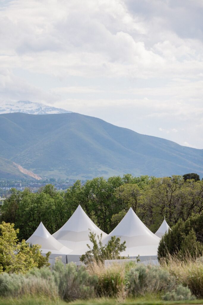 Elegant outdoor wedding reception beneath a white tent with mountain views, green linens, and wooden chairs, planned by Shellie Ferrer Events.