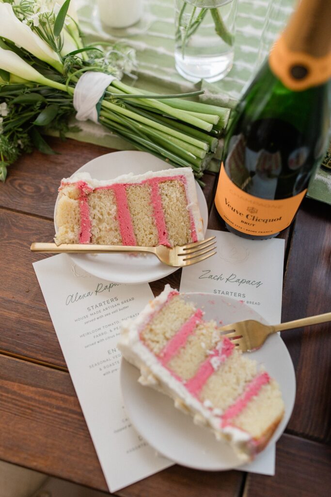 Slices of wedding cake with pink filling, champagne, a bridal bouquet, and personalized menus at a reception planned by Shellie Ferrer Events.